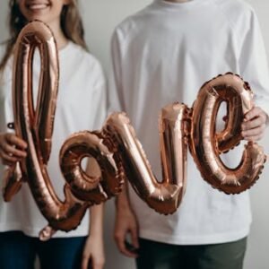 A couple in white t-shirts holding a metallic 'love' balloon, expressing joy and affection.