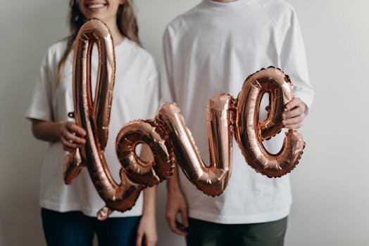 A couple in white t-shirts holding a metallic 'love' balloon, expressing joy and affection.